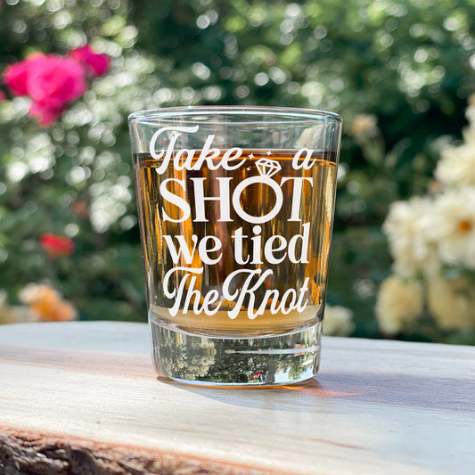 Etched shot glass with 'take a shot we tied the knot' phrase, ideal for wedding celebrations with roses in background